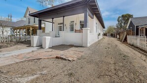 Een huis met een overdekte patio, een pad van bakstenen en een witte picket hek.