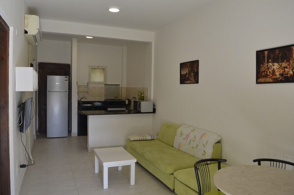 A compact living space with a kitchenette, a green sofa, a small table, and two chairs.