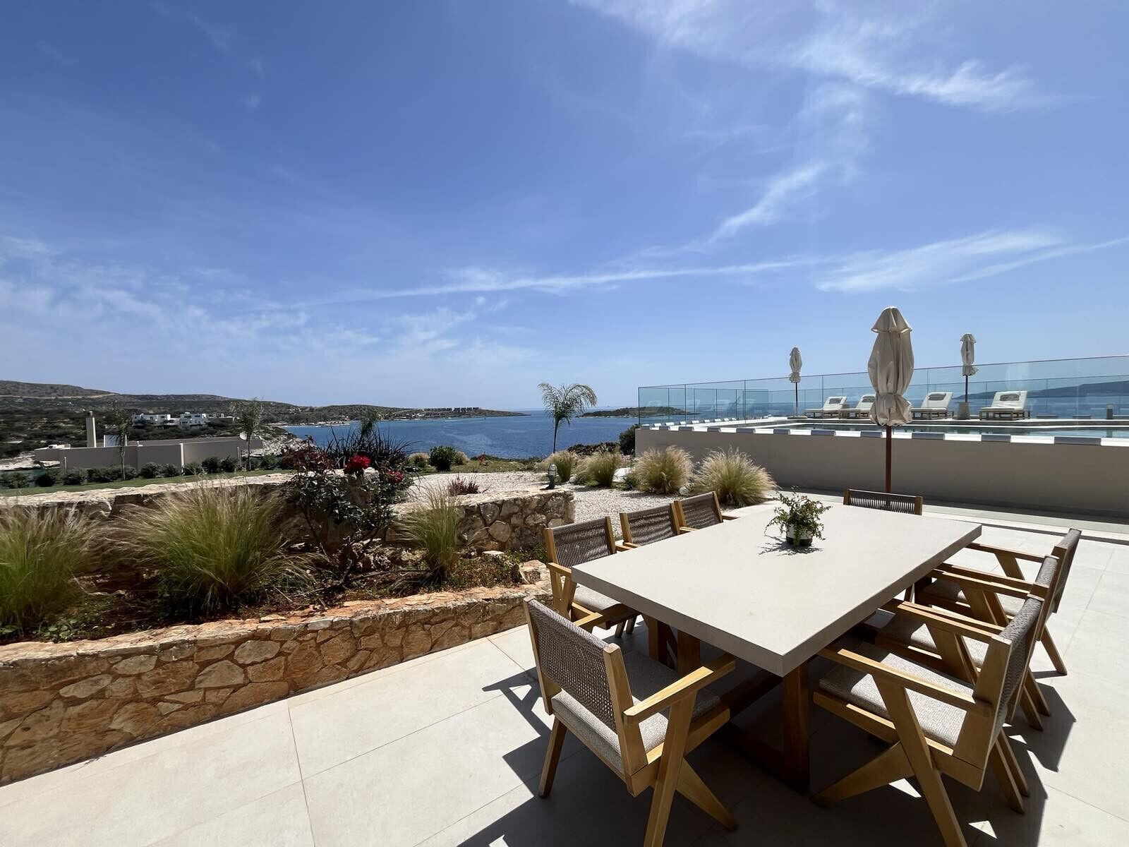 Um terraço com mesa e cadeiras, com vista para a paisagem costeira sob um céu claro.