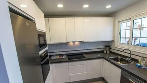 A modern kitchen with white cabinets, a stainless steel refrigerator, a built-in oven, and a window with a view. - Casa Bill - Firepit Nights by Villas Now (Playa Blanca)