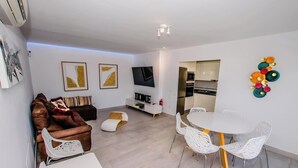 A modern living room with a sofa, a dining table with chairs, a TV, and a kitchen area. - Casa Bill - Firepit Nights by Villas Now (Playa Blanca)