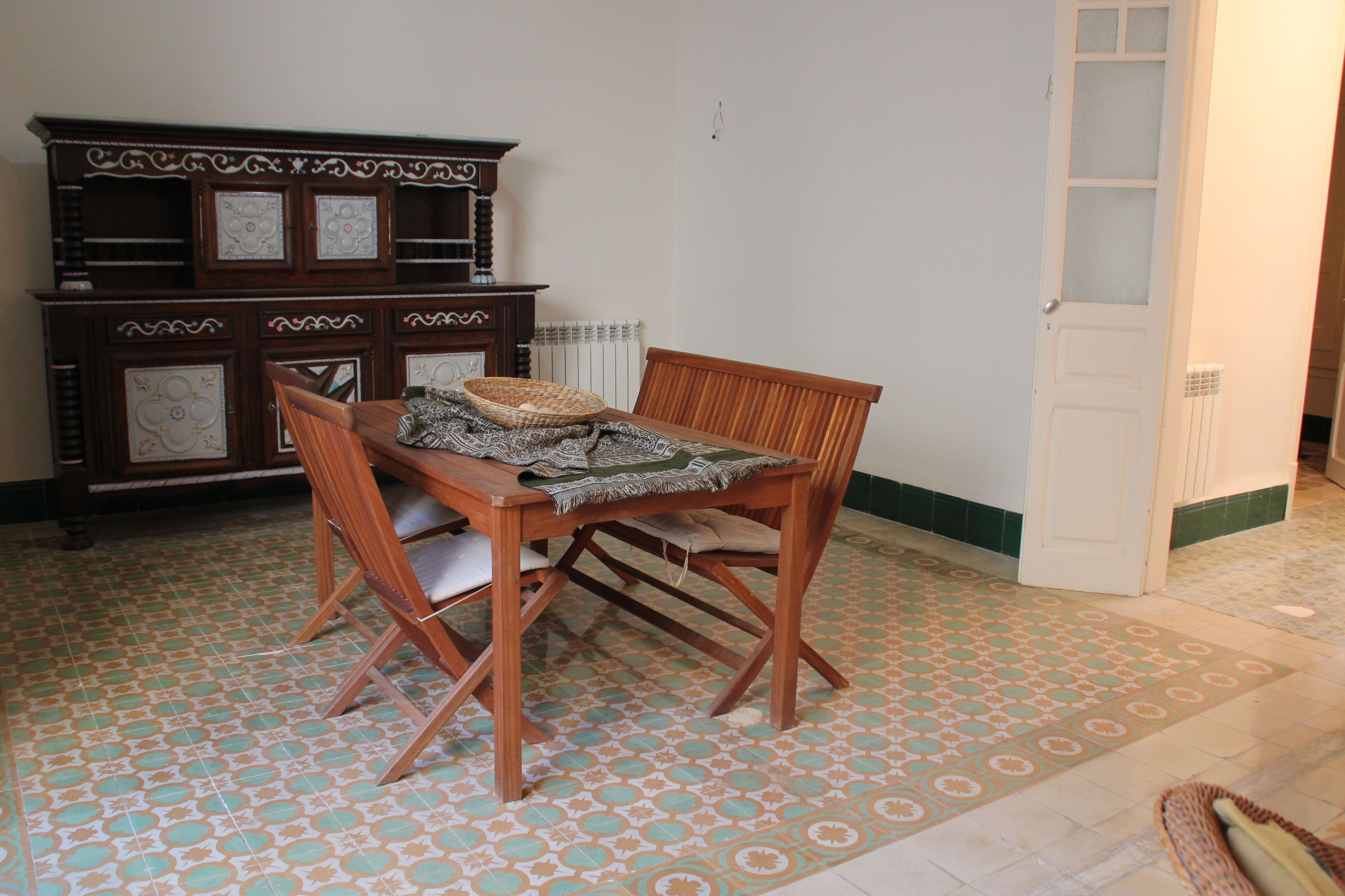 A dining area with a wooden table and chairs, a patterned floor, and a cabinet with decorative panels.