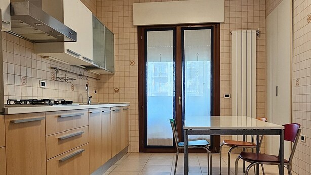 Une cuisine avec des meubles de rangement en bois, une cuisinière à gaz et une table à manger avec des chaises.