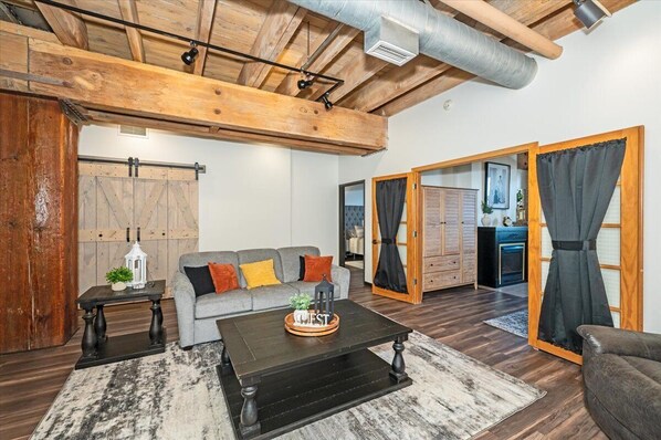 A cozy living room with a wooden ceiling, a gray sofa with orange cushions, a black coffee table, and a rustic wooden door. - Lake Superior Loft - Sleeps 10, Heart of Canal Park, Lake Superior View (Duluth)