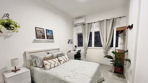 Un dormitorio con cama, mesita de noche, lámpara y una planta en maceta.