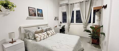 A bedroom with a bed, bedside table, lamp, and a potted plant.