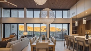 Un comedor amplio con una mesa grande dispuesta para seis comensales, un sofá y una zona de cocina con armarios de madera e iluminación colgante.