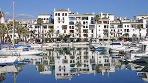 A marina with boats docked, surrounded by white buildings with balconies and palm trees.