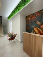 Un espace d’accueil moderne agrémenté d’un jardin vertical verdoyant, d’un comptoir de réception et d’une fresque représentant des feuilles tropicales.