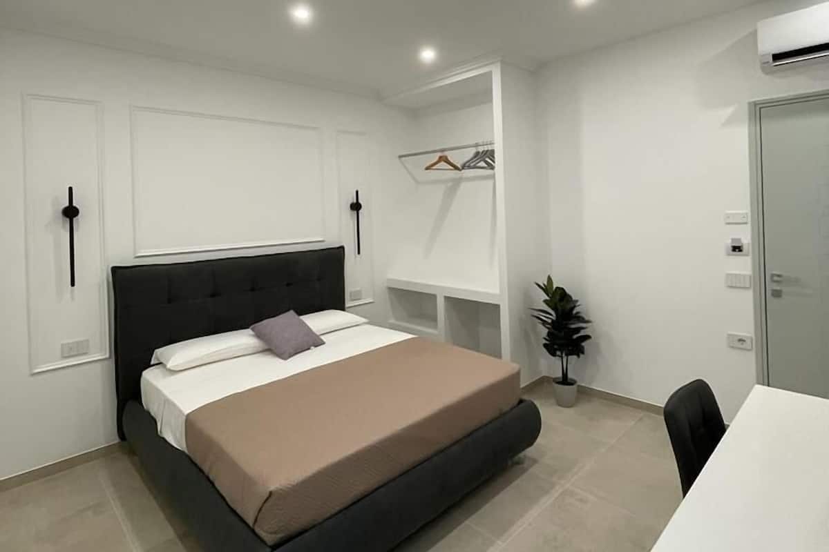 A modern bedroom with a bed, bedside tables, a desk, and a potted plant.