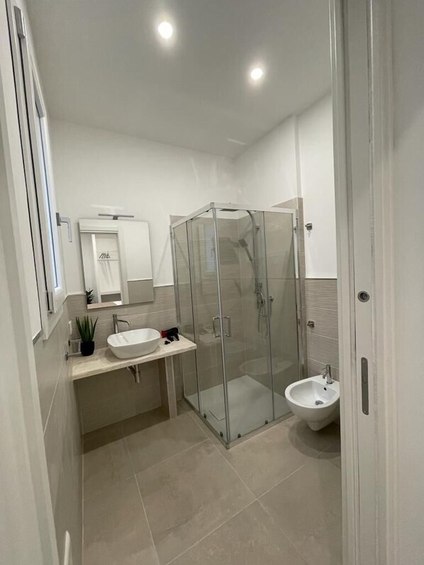 Un baño moderno con ducha acristalada, lavamanos y un bidé.
