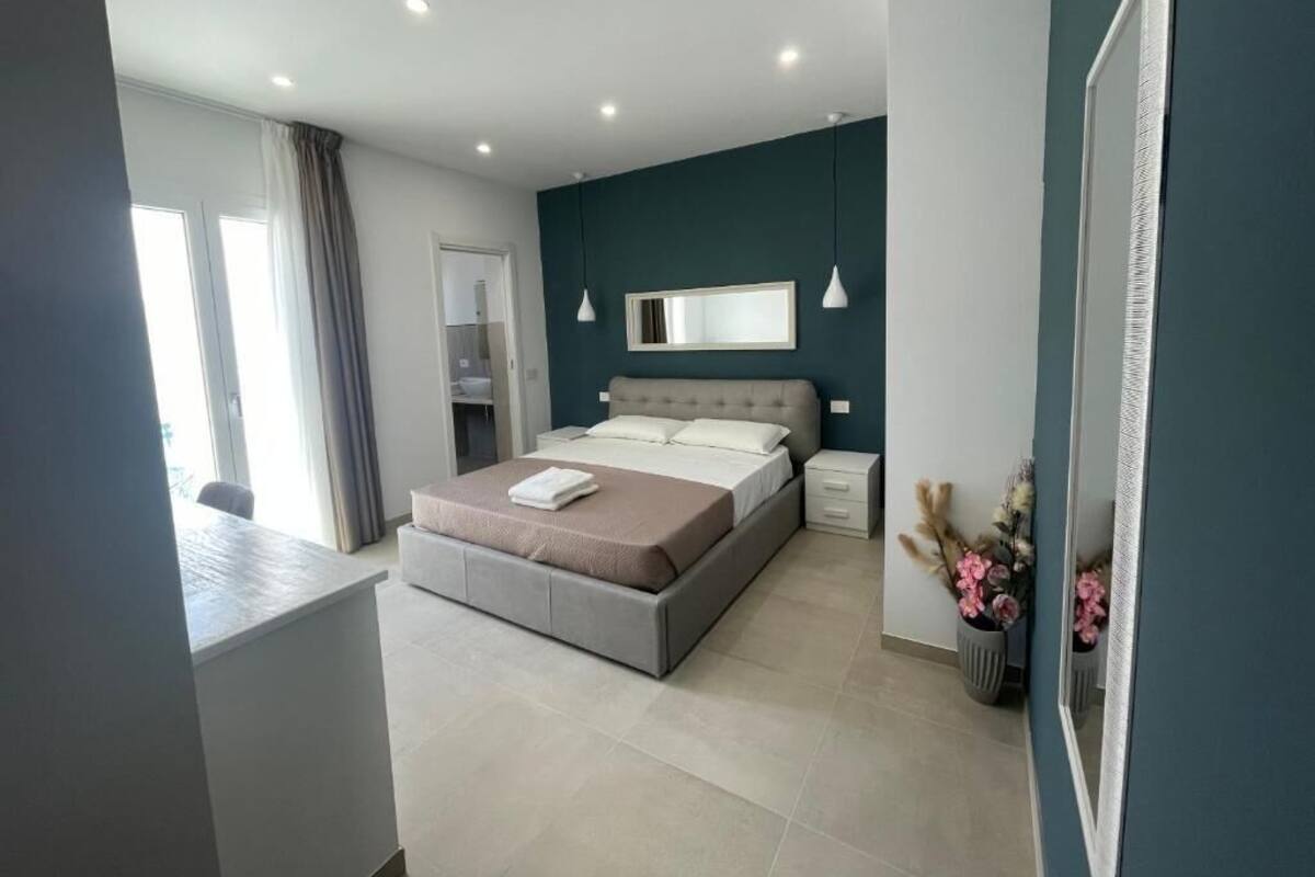 A modern bedroom with a bed, bedside tables, a mirror, and a window with curtains.