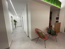 Un couloir moderne agrémenté d’un mur vert, de deux fauteuils rouges avec des coussins et d’un sol carrelé.
