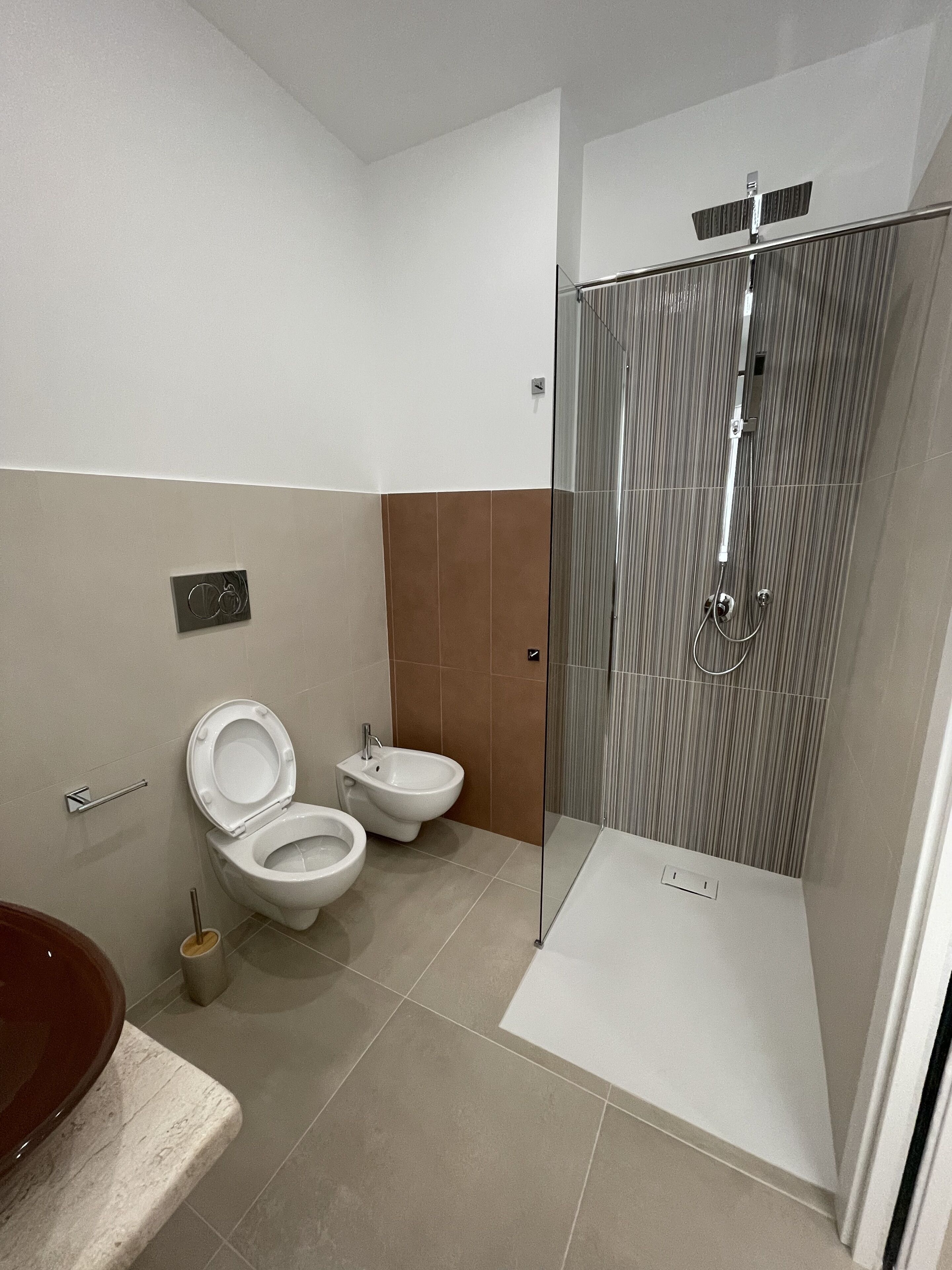 Een moderne badkamer met toilet, bidet en een douchecabine met glazen wanden.