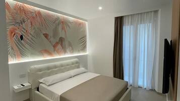 Une chambre moderne avec un grand lit, une table de chevet, un téléviseur fixé au mur et une fenêtre avec des rideaux.