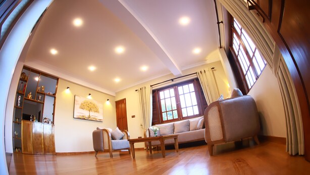 A spacious living room with wooden flooring, a sofa, a chair, and a coffee table. There is a window with curtains and a door in the background. - Golden Shower Inn (Kandy)