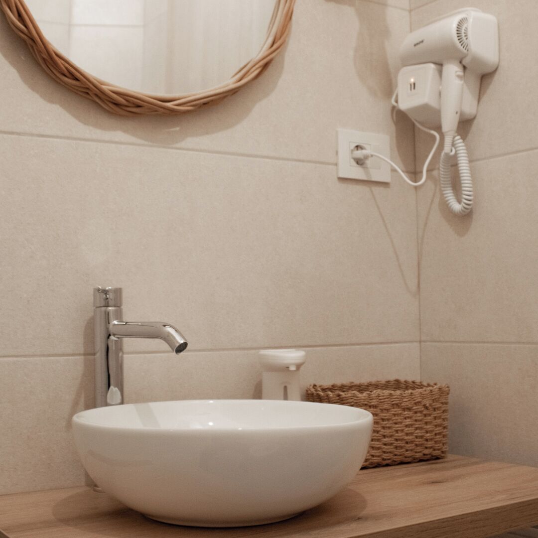 A bathroom with a white sink, a round mirror, a hairdryer on the wall, and a wicker basket on the counter.