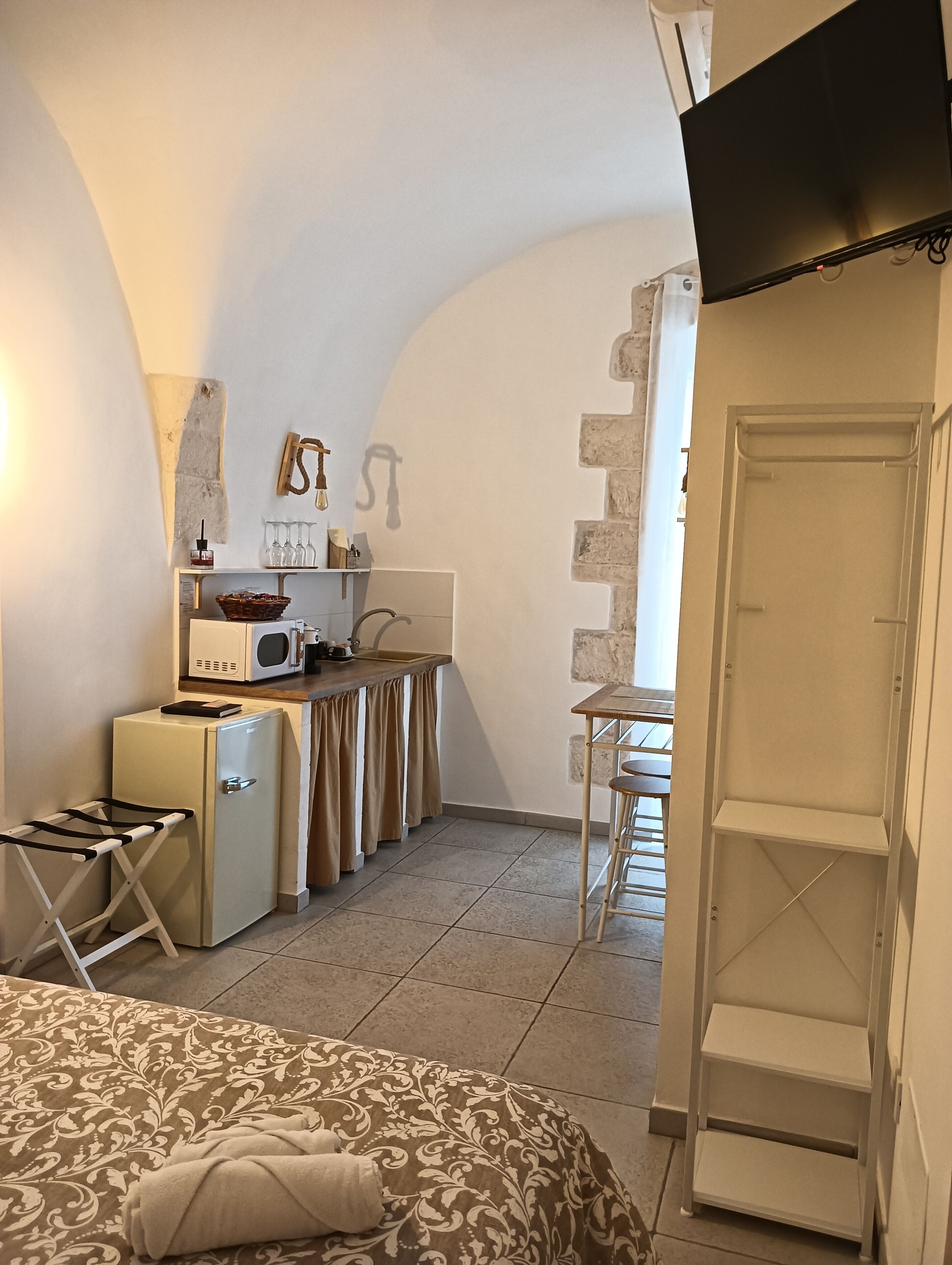 A compact kitchen with a refrigerator, microwave, and sink, a small dining area with stools, and a wardrobe with a mirror.
