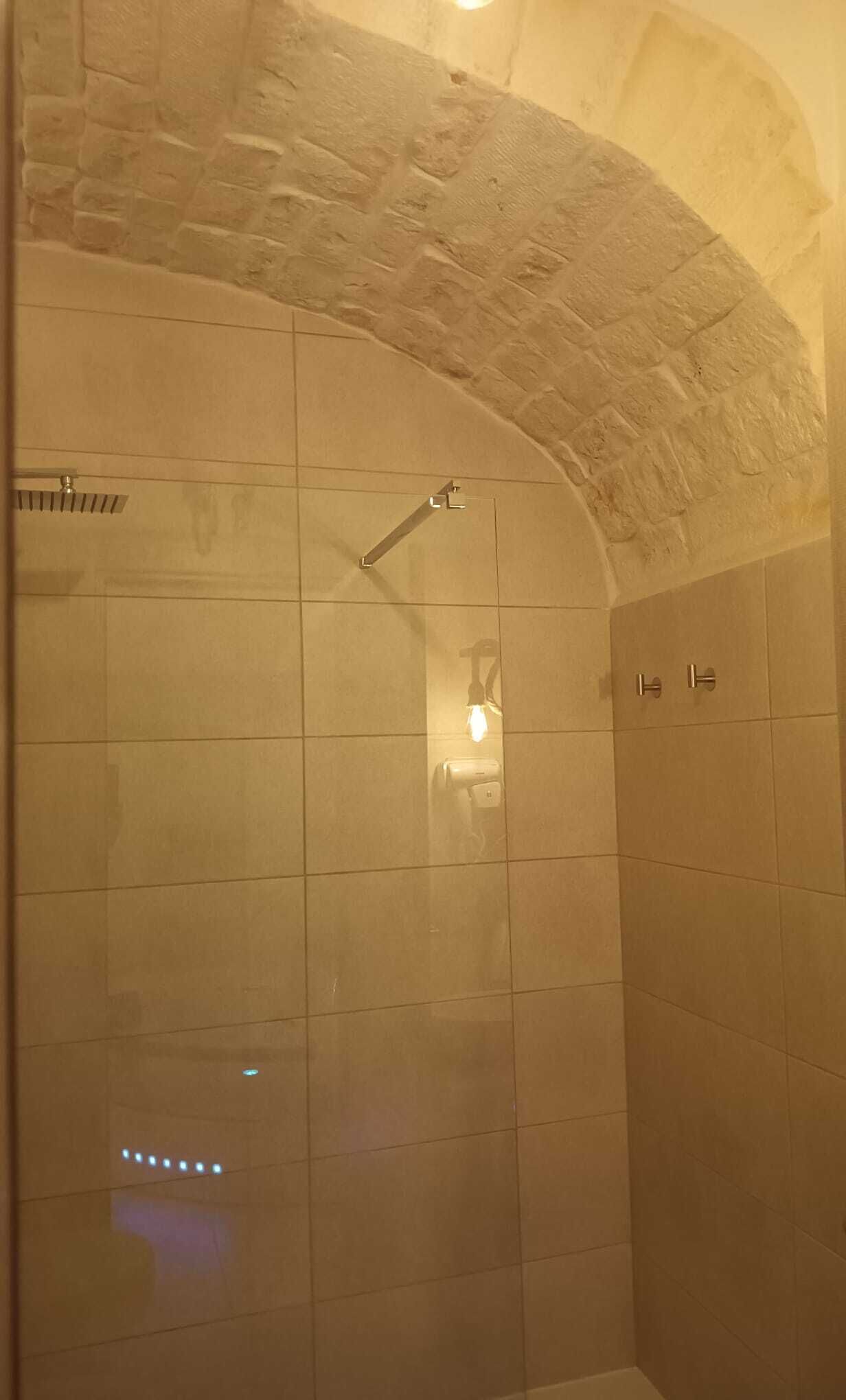 Eine Dusche mit Steinbogen-Decke, gefliesten Wänden und einer Handbrause.