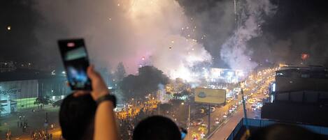 A nighttime view of a city street with fireworks, a crowd, and a person taking a photo.