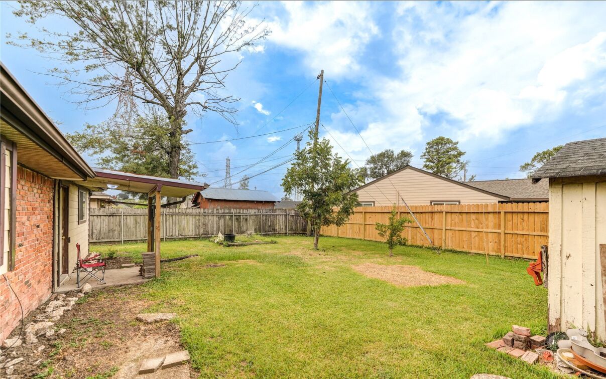 A backyard with a wooden fence, a brick house, and a covered patio area. - Perfect home away from home. Excellent weekend getaway. (Houston)