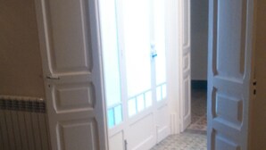 Une pièce avec un sol à motifs, un lit recouvert d’une couverture bleue et une porte donnant sur une autre pièce.