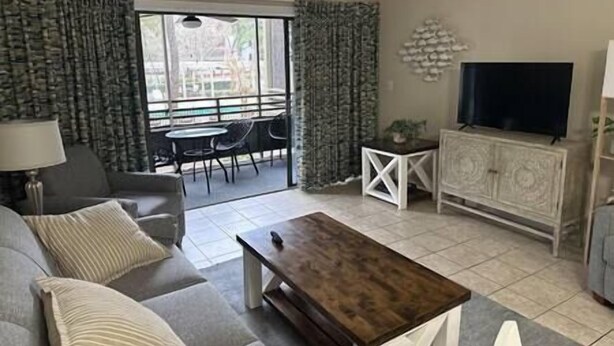 A living room with a sofa, coffee table, TV, and a balcony with chairs and a table. - Beautiful Condo in Ocean Creek (Horry County)