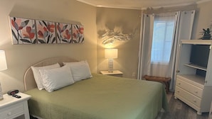 A neatly arranged bedroom with a bed, bedside table, lamp, and a TV stand. - Beautiful Condo in Ocean Creek (Horry County)