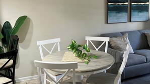 A dining area with a round table, white chairs, a ceiling fan, and two abstract paintings on the wall. - Beautiful Condo in Ocean Creek (Horry County)