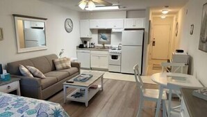 Un espacio habitable compacto con kitchenette, un sofá, una mesa de centro y una zona de comedor.