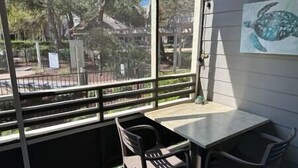 Un pequeño espacio al aire libre con una mesa y sillas, vista a árboles y un edificio en el fondo, y un cuadro de una tortuga en la pared.