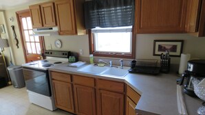 Une cuisine avec des meubles de rangement en bois, une cuisinière, un évier et une fenêtre avec des stores.