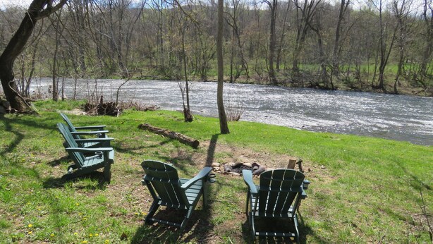 Un espace de pique-nique au bord de la rivière, avec des chaises Adirondack vertes et un foyer.
