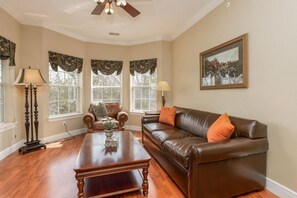 A living room with a brown leather sofa, a wooden coffee table, and a chandelier. There are two windows with curtains and a painting on the wall. - Stylish 1BR Urban Haven: Great Rock Retreat (Branson)