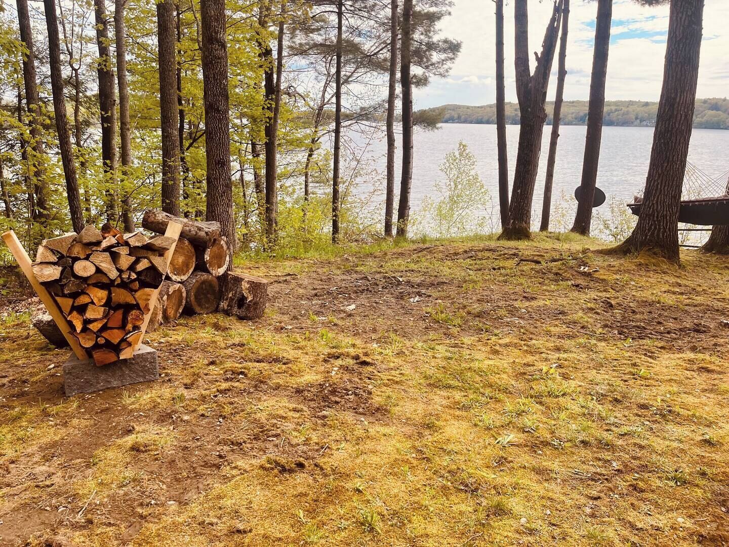 A lakeside view with a stack of firewood and a bench.