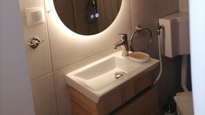 Un baño moderno con un espejo ovalado grande, un lavabo blanco, tocador de madera y zona de ducha.