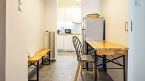 Una cocina estrecha con una mesa y un banco de madera, un refrigerador y un microondas.
