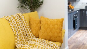 A yellow sofa with a patterned throw blanket and two pillows. - Open Mind Property - Luxury 5 Beds & Free Parking (Portsmouth)