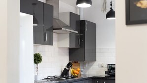A modern kitchen with dark grey cabinets, a stainless steel range hood, and a gas stove. There is a small potted plant on the counter and a fruit bowl with oranges and bananas. - Open Mind Property - Luxury 5 Beds & Free Parking (Portsmouth)