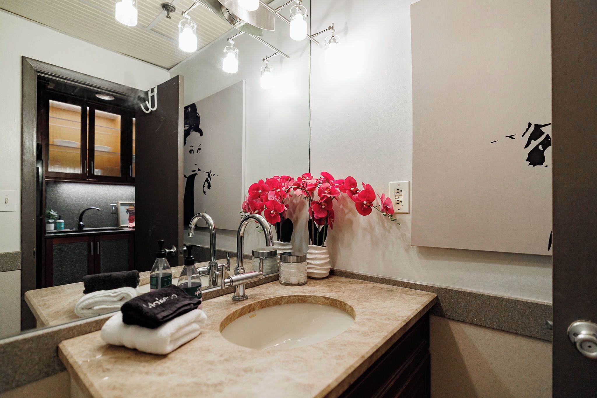 Une salle de bain moderne avec un grand miroir, un lavabo et un vase rempli de fleurs rouges.