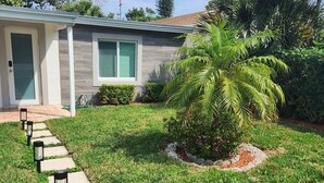 A residential property with a well-maintained lawn, a stone pathway leading to the front door, and a small palm tree in the yard. - Boca Jewels with Heated Jacuzzi (Boca Raton)