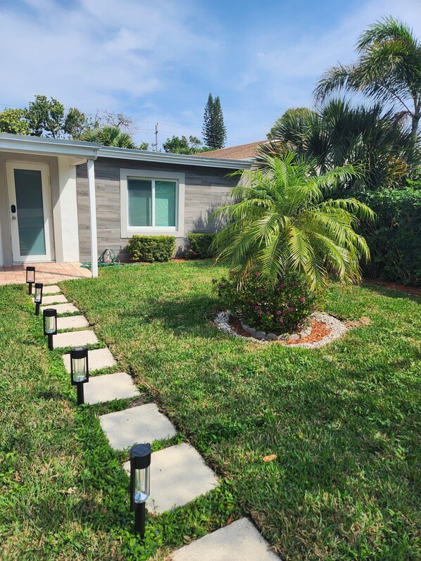 A residential property with a well-maintained lawn, a stone pathway leading to the front door, and a small palm tree in the yard. - Boca Jewels with Heated Jacuzzi (Boca Raton)