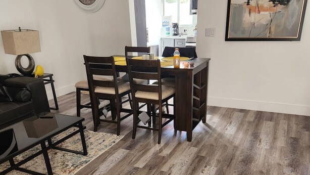 A dining area with a wooden table and chairs, a clock on the wall, and a painting. - Boca Jewels with Heated Jacuzzi (Boca Raton)