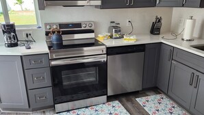 A modern kitchen with grey cabinets, stainless steel appliances, and a dog on a star-patterned mat. - Boca Jewels with Heated Jacuzzi (Boca Raton)