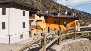 Ein traditionelles Chalet mit einer Steintreppe, die zu einem Holzbalkon führt, vor einer Bergkulisse.