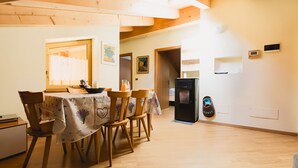 Ein Essbereich mit einem Tisch für vier Personen, Holzstühlen, einem schwarzen Kühlschrank und einem an der Wand befestigten Schuhregal mit dem Aufdruck 'GÄSTE'.