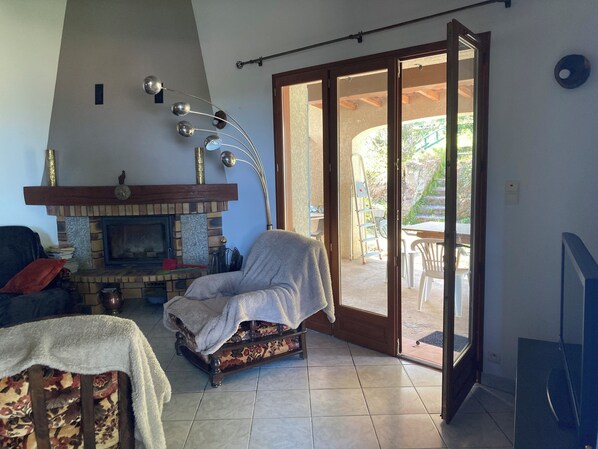 A living room with a fireplace, a covered chair, a sofa, and a sliding glass door leading to an outdoor area.