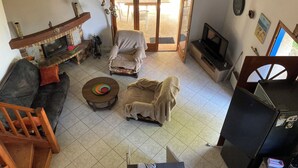 Un salon avec une cheminée, un canapé, un fauteuil, une télévision et une vue sur l’extérieur.