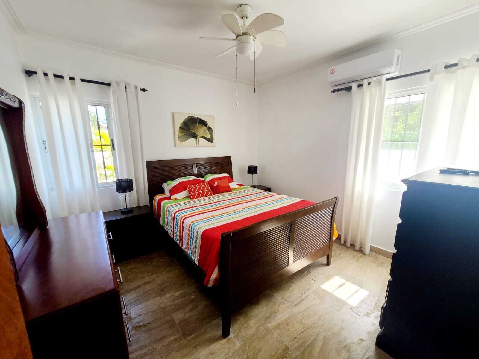 Un dormitorio con una cama de madera, ventilador de techo, escritorio y cómoda.