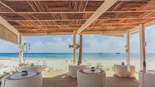An outdoor seating area with round tables and white chairs, overlooking a beach and ocean. - Magic Cortesea luxury beach (Punta Cana)